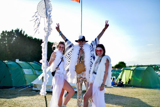 Image shows a group of friends at a festival, wearing extravagant clothing while standing in front of tents. 